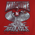 2004 vintage NCAA University of Nebraska-Lincoln Cornhuskers spell-out Gildan T-Shirt. Red in color with "Rise of the Machine, West Coast Offense" text and football player graphic on front by Art-Fx Collectors Edition. X-Large in size and in excellent condition.