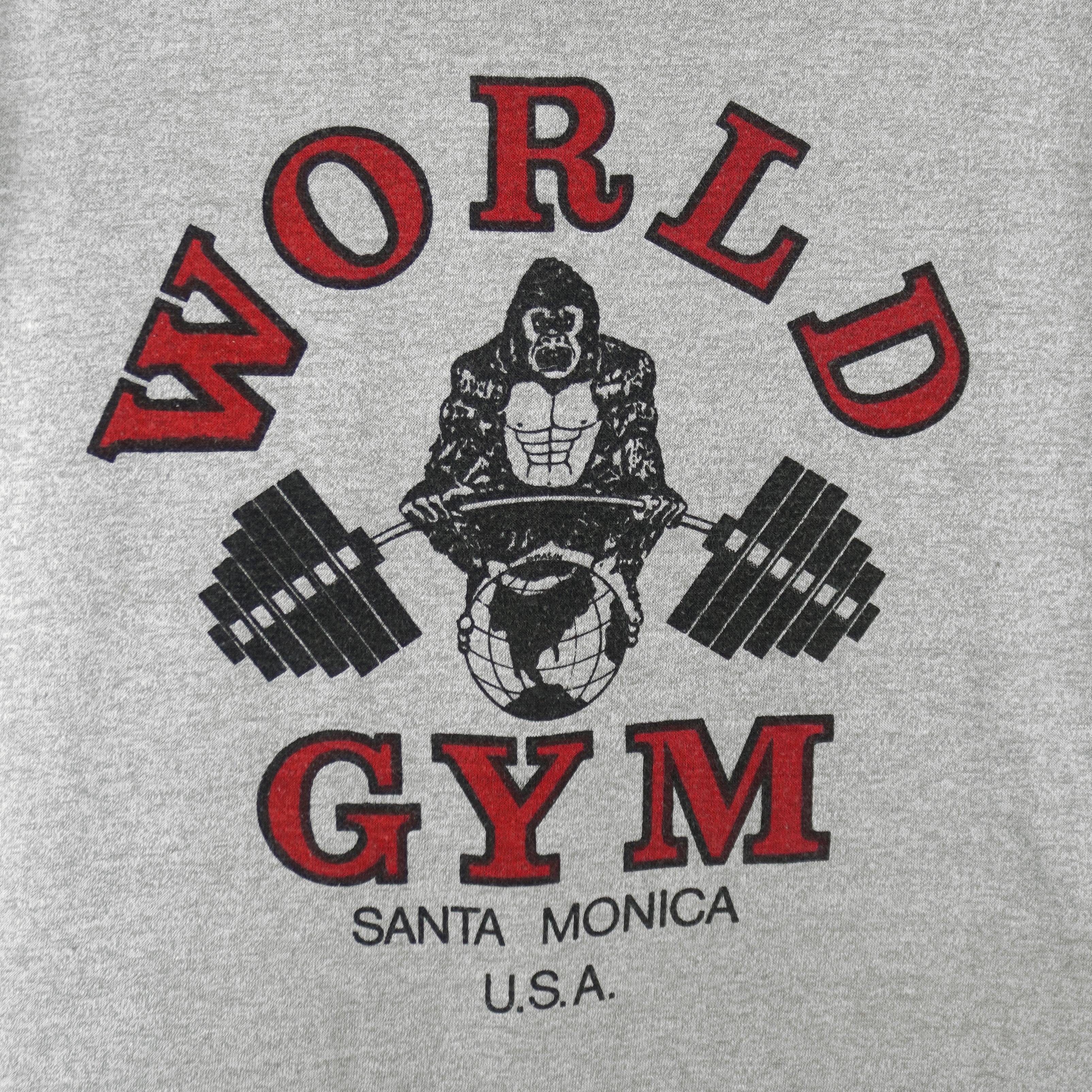 1990s vintage World Gym, Santa Monica USA sleeveless workout shirt. Grey in color with black trim, has a big printed graphic of the gorilla logo on front and back, fits Medium in size, and is in excellent condition.