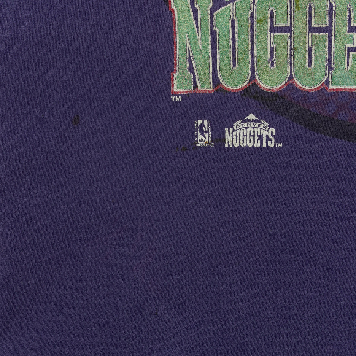 Close-up of dark marks and small holes below the Denver Nuggets logo