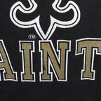 Close-up of cracking and wear in the Saints wordmark and fleur-de-lis print on the black T-shirt.