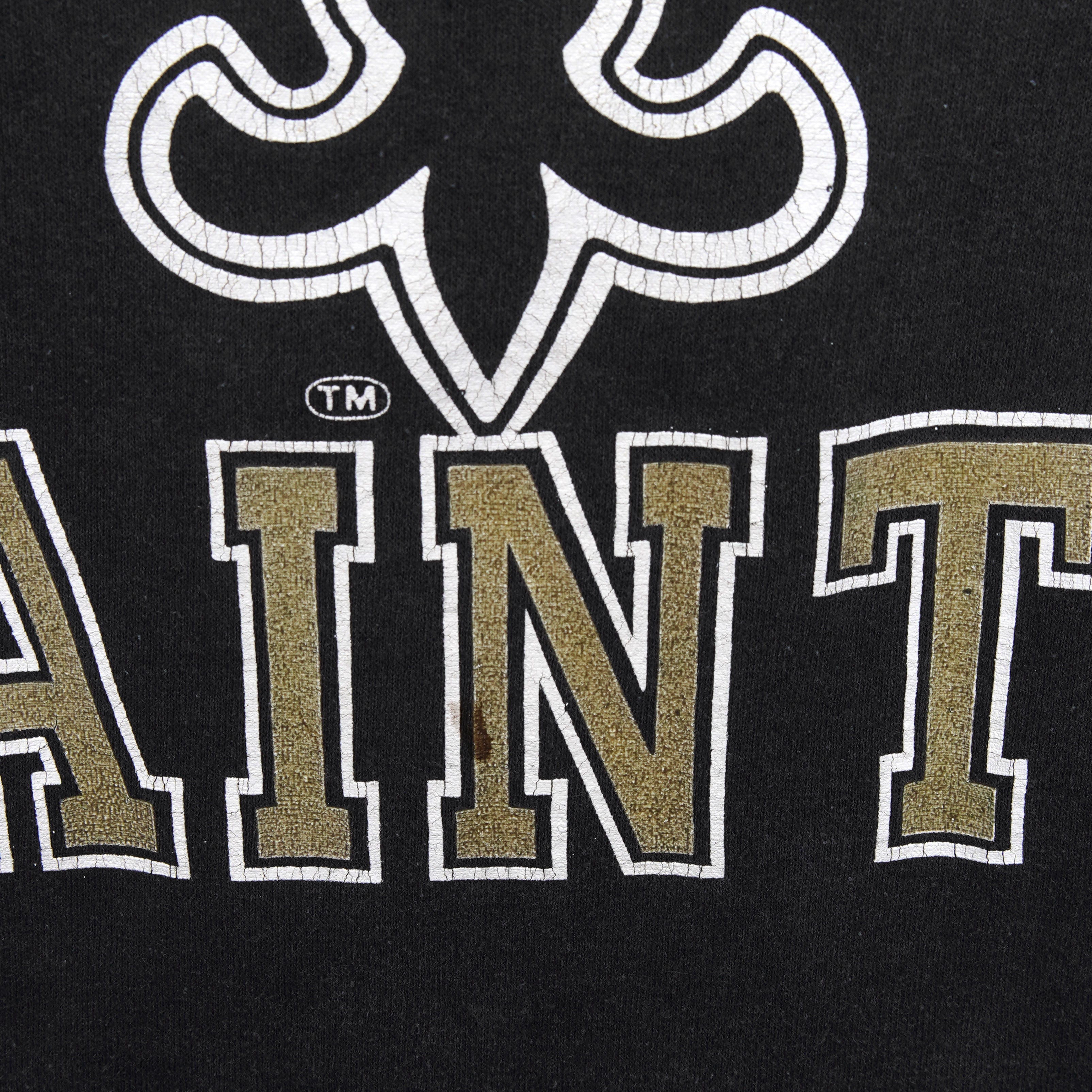 Close-up of cracking and wear in the Saints wordmark and fleur-de-lis print on the black T-shirt.