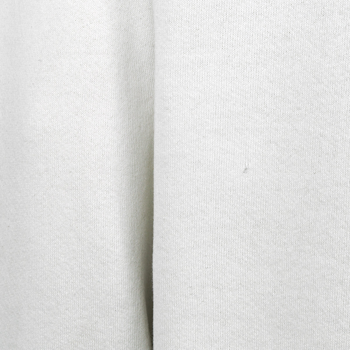 Close-up of a small hole and mark on the white sweatshirt fabric.